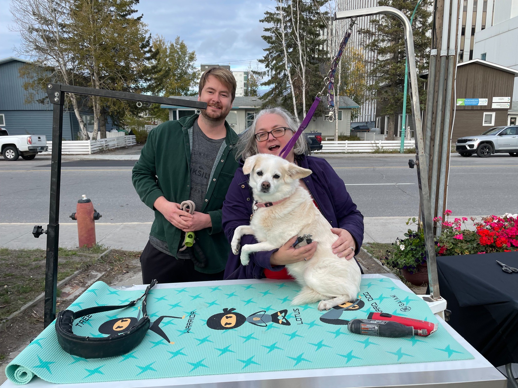 People with white dog on grooming table outdoors.