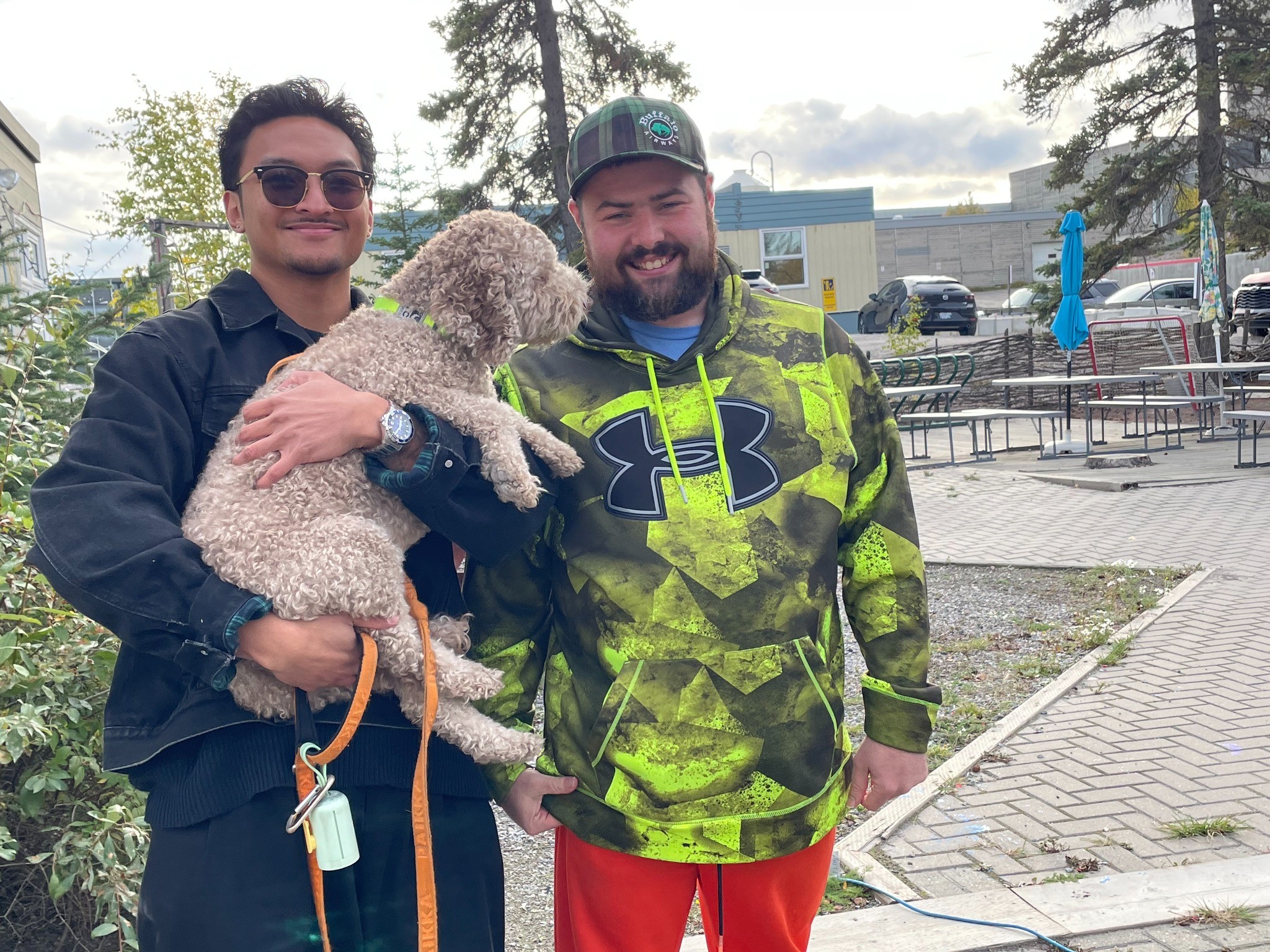Two men outdoors, one holding a dog. Two men outdoors, one holding a dog.